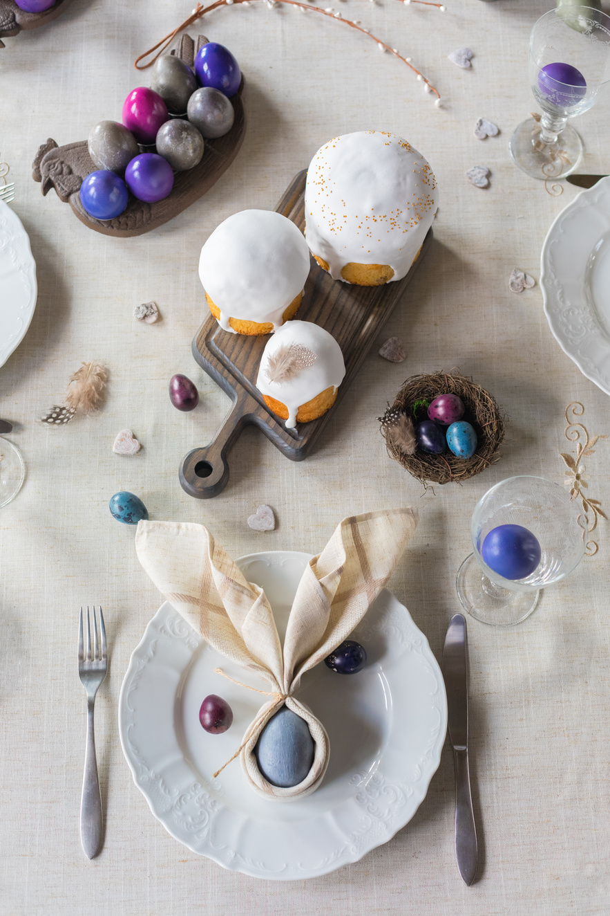 Easter festive spring table setting decoration, bunny ears shaped napkins, dyed eggs, cakes, flowers, selective focus